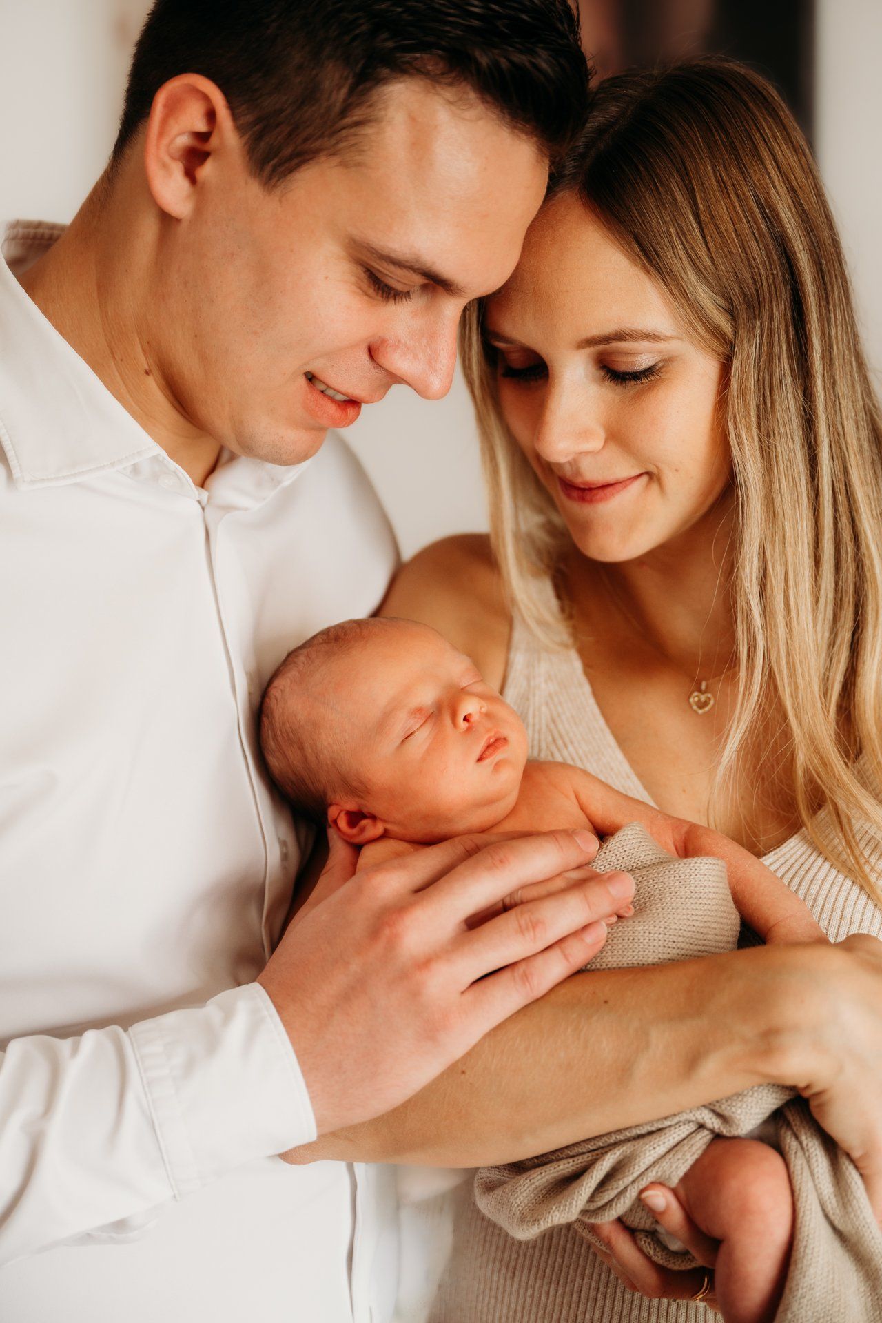 Junge Familie hält ihr Neugeborenes liebevoll im Arm